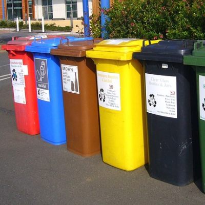 6 colourfull wheelie bins on a sidewalk/pavement